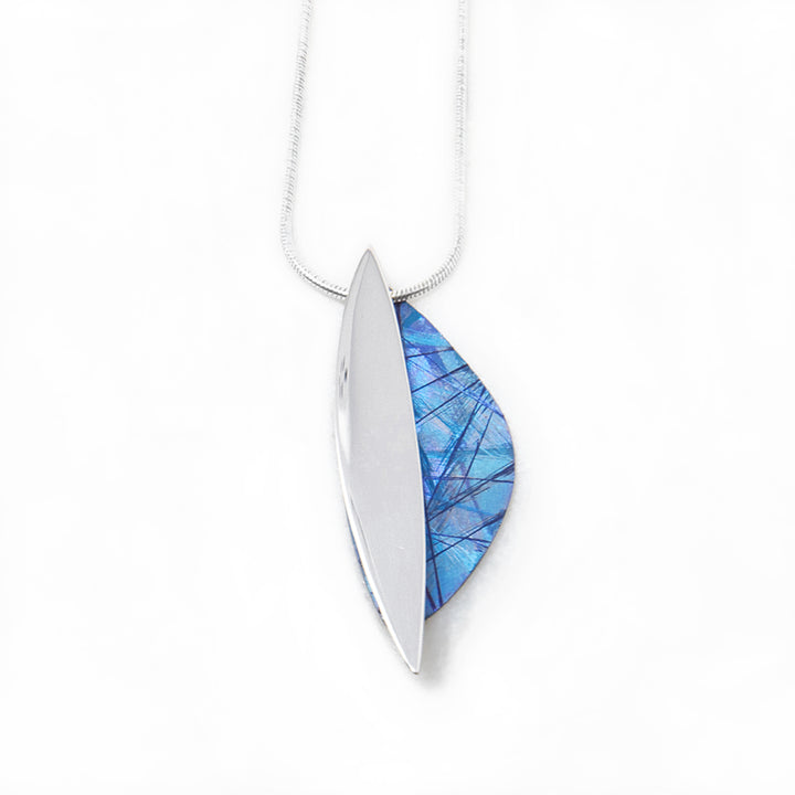 This unique titanium necklace pendant is made form sterling silver and anodized titanium. The piece have a thin, vertical oval piece made from silver with a crescent piece on the side made from titanium. The titanium piece is blue and has colorful designs on the surface of it achieved by anodizing the metal.
