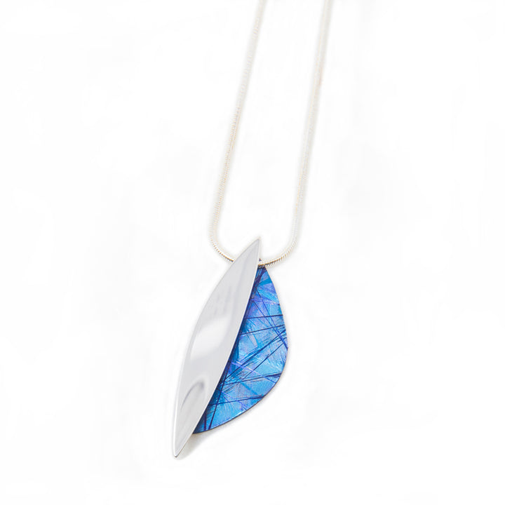This unique titanium necklace pendant is made form sterling silver and anodized titanium. The piece have a thin, vertical oval piece made from silver with a crescent piece on the side made from titanium. The titanium piece is blue and has colorful designs on the surface of it achieved by anodizing the metal.