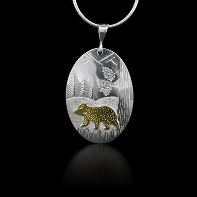 This sterling silver bear pendant is oval shaped and has a 10K gold bear. There are carvings that depict a bear and a forest scene.