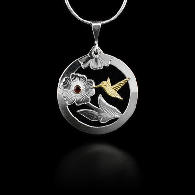 This sterling silver circle hummingbird pendant is cutout around a hummingbird and flower. The hummingbird is made of 10K gold and their is a garnet gem in the center of the flower. There are also carvings depicting the flower and hummingbird on the pendant.