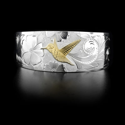 This sterling silver cuff bracelet has carvings that depict the Hummingbird and flowers. The Hummingbird is made of 10K gold.