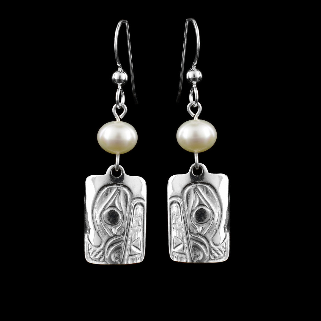 These dangling teardrop earrings have rectangle shaped hangs cast from sterling silver. There is a single, white pearl below the hooks and above the hangs. The head of the Bear is cast into the hangs and its snout is facing down. The eyes and head are large and take up most of the hangs with the teeth below them.