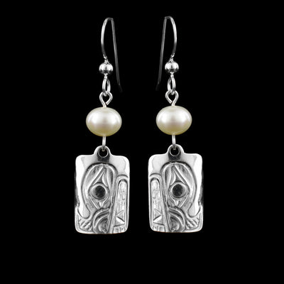 These dangling teardrop earrings have rectangle shaped hangs cast from sterling silver. There is a single, white pearl below the hooks and above the hangs. The head of the Bear is cast into the hangs and its snout is facing down. The eyes and head are large and take up most of the hangs with the teeth below them.