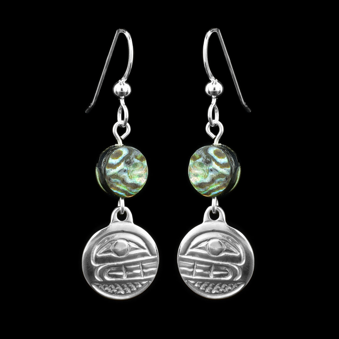 These abalone drop earrings silver have small, circle hangs made from sterling silver. Below the hooks is a single, round abalone shell charm with the hangs dangling from them. On the hangs, the head of the Orca is shown at a side profile with its teeth and eyes detailed. There are cross hatching designs in the background of the portrait.