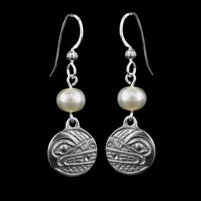 These dangling pearl earrings silver have small, circle hangs made from sterling silver. Below the hooks is a single, white pearl with the hangs dangling from them. On the hangs, the head of the Wolf is shown at a side profile with its teeth, eyes and nose detailed. There are cross hatching designs in the background of the portrait.