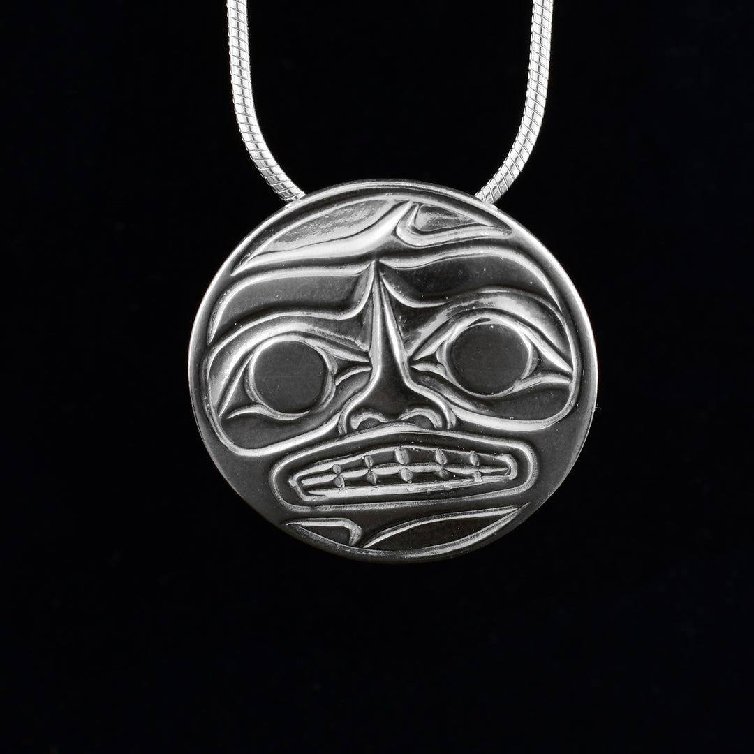 This sterling silver Moon pendant has a circle shape with a depiction of the Moon legend cast into it. The face of the Moon is shown with its eyes, eyebrows, nose, teeth and mouth detailed.