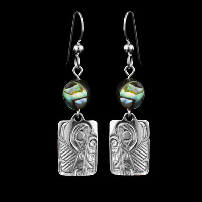 These abalone drop earrings silver have small, rectangle hangs made from sterling silver. Below the hooks is a single, round abalone shell charm with the hangs dangling from them. On the hangs, the head of the Wolf is shown at a side profile with its teeth, nose, ears and eyes detailed. There are fine, line designs in the background of the portrait.