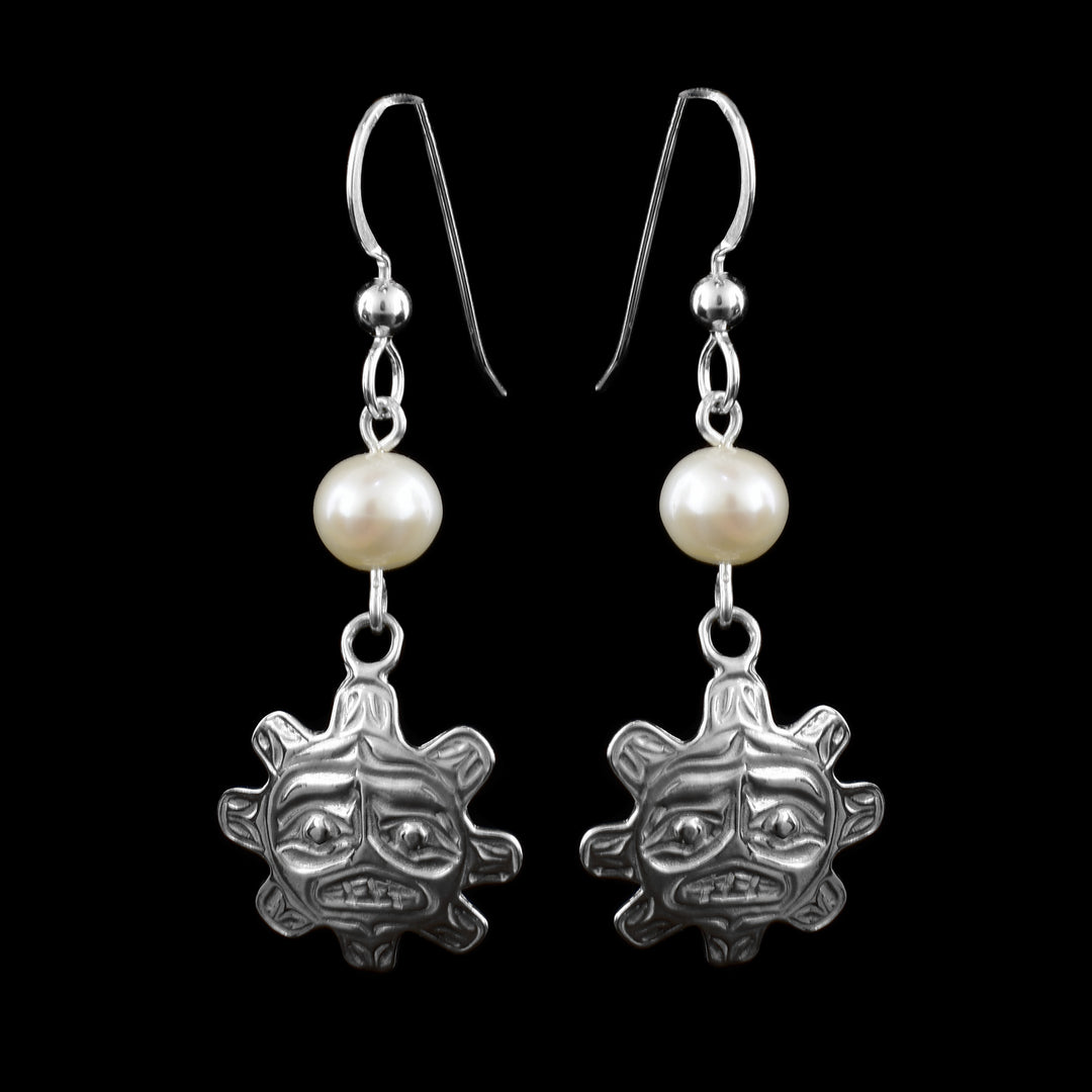 These sterling silver pearl drop earrings has white, freshwater pearls dangling from the long hooks. The hangs are round and have knobs extending from it imitating sun rays. The hangs dangle from the pearls and have features of the face of the sun cast into them including the eyebrows, eyes, and mouth.