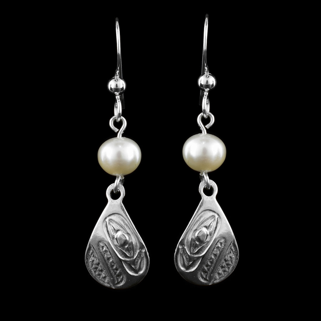 These dangling teardrop earrings have teardrop shaped hangs cast from sterling silver. There is a single, white pearl below the hooks and above the hangs. The head of the Raven is cast into the hangs at a side profile with its beak facing down. The beak and eye are large and takes up most of the hangs. There are cross hatching designs in the background of the portrait.