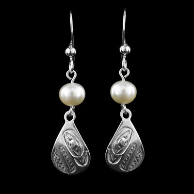 These dangling teardrop earrings have teardrop shaped hangs cast from sterling silver. There is a single, white pearl below the hooks and above the hangs. The head of the Raven is cast into the hangs at a side profile with its beak facing down. The beak and eye are large and takes up most of the hangs. There are cross hatching designs in the background of the portrait.