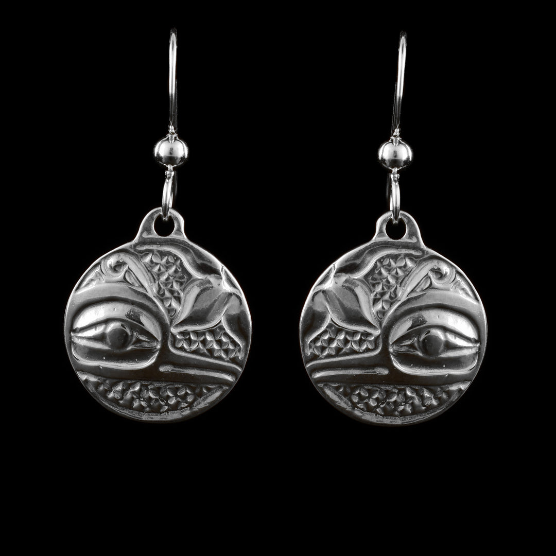 These sterling silver dangle Hummingbird earrings have circle shaped hangs dangling from long hooks. The hangs depict the side profile of the head of the Hummingbird with its eye and thin beak detailed. There are three flower petals above its head and cross hatching designs in the background.