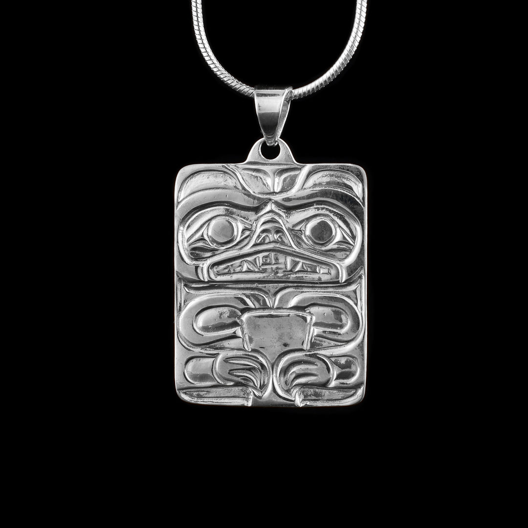 This sterling silver Bear pendant has a wide, rectangle shape and a depiction of the Bear has been cast into it. The head of the Bear takes up the top half of the pendant and shows its ears, eyes, nose and open mouth that exposes its teeth. At the bottom is its chest and arms with claws.
