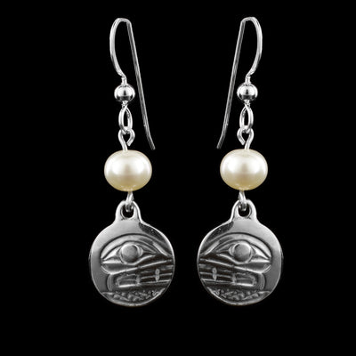 These dangling pearl earrings silver have small, circle hangs made from sterling silver. Below the hooks is a single, white pearl with the hangs dangling from them. On the hangs, the head of the Orca is shown at a side profile with its eye and teeth detailed. There are cross hatching designs in the background of the portrait.