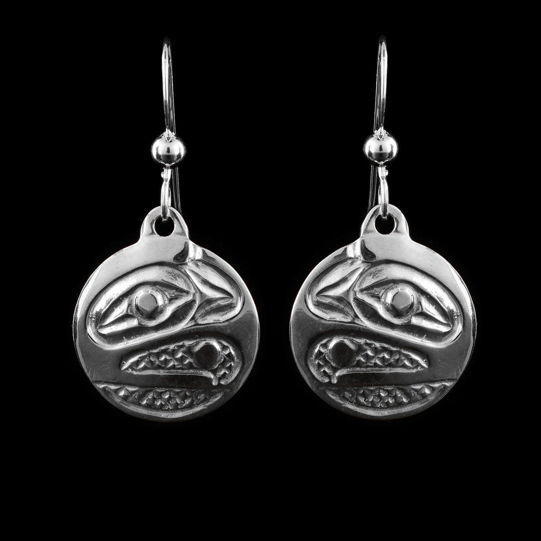 These Raven earrings have small, sterling silver hangs attached to hooks. The head of the Raven carved at a side profile into the hangs. Its eyes and beak are visible and there are cross hatching designs in the background of the portrait.