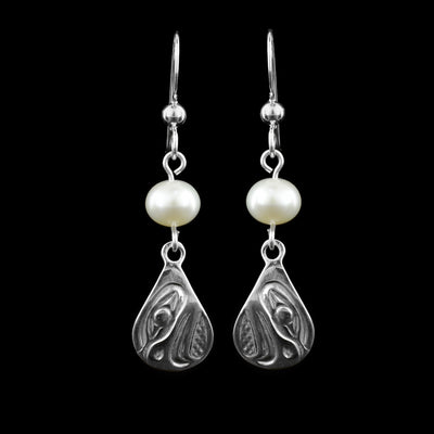 These dangling teardrop earrings have teardrop shaped hangs cast from sterling silver. There is a single, white pearl below the hooks and above the hangs. The head of the Eagle is cast into the hangs and its beak is facing down. The beak is large, curves down at the end and takes up most of the hangs. There are cross hatching designs in the background of the portrait.