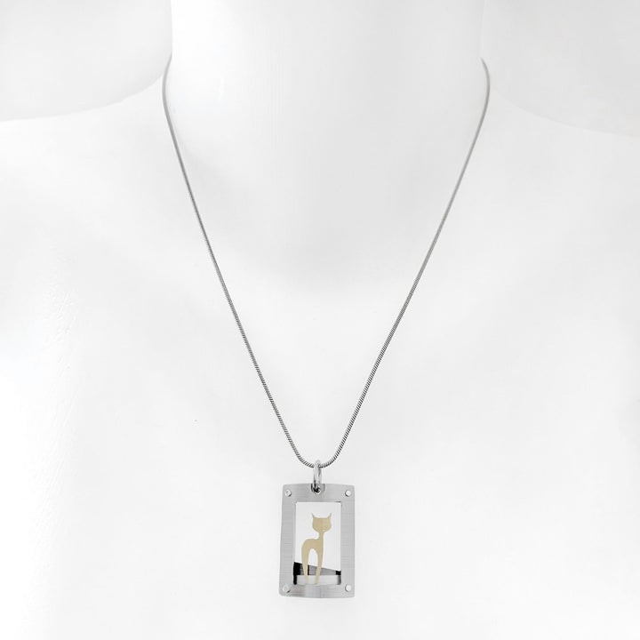 This cat necklace with pendant has a curved, grey frame with gold-colour cat silhouette inside. Side-view of cat with head turned to side so both ears are visible. Minimalist design. By JR Franco. Stainless steel snake chain included.