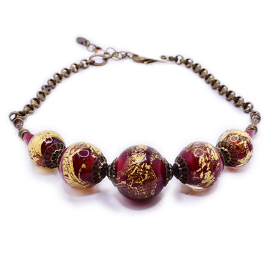 Brass necklace with large, round, handmade lampworked glass beads along front. Beads are translucent and red with 23K gold leaf.