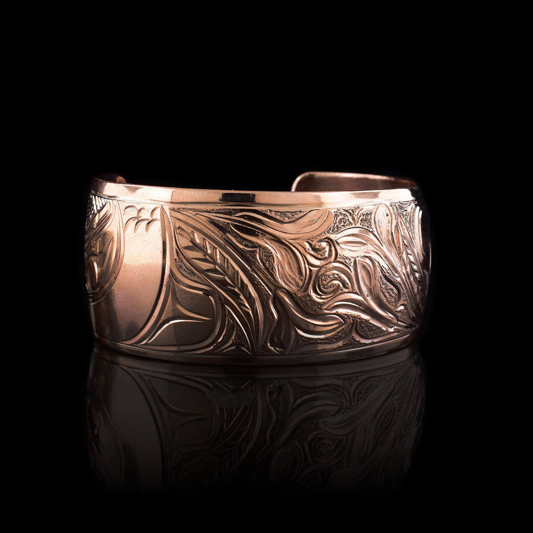 This chunky copper cuff bracelet features a bold and detailed engraving of an eagle, a symbol of strength and vision. The eagle's head is prominently displayed on one side, with finely carved feathers and textured detailing. The rest of the bracelet is adorned with flowing, organic patterns that enhance the richness and movement of the design. With its wide band and warm copper tones.