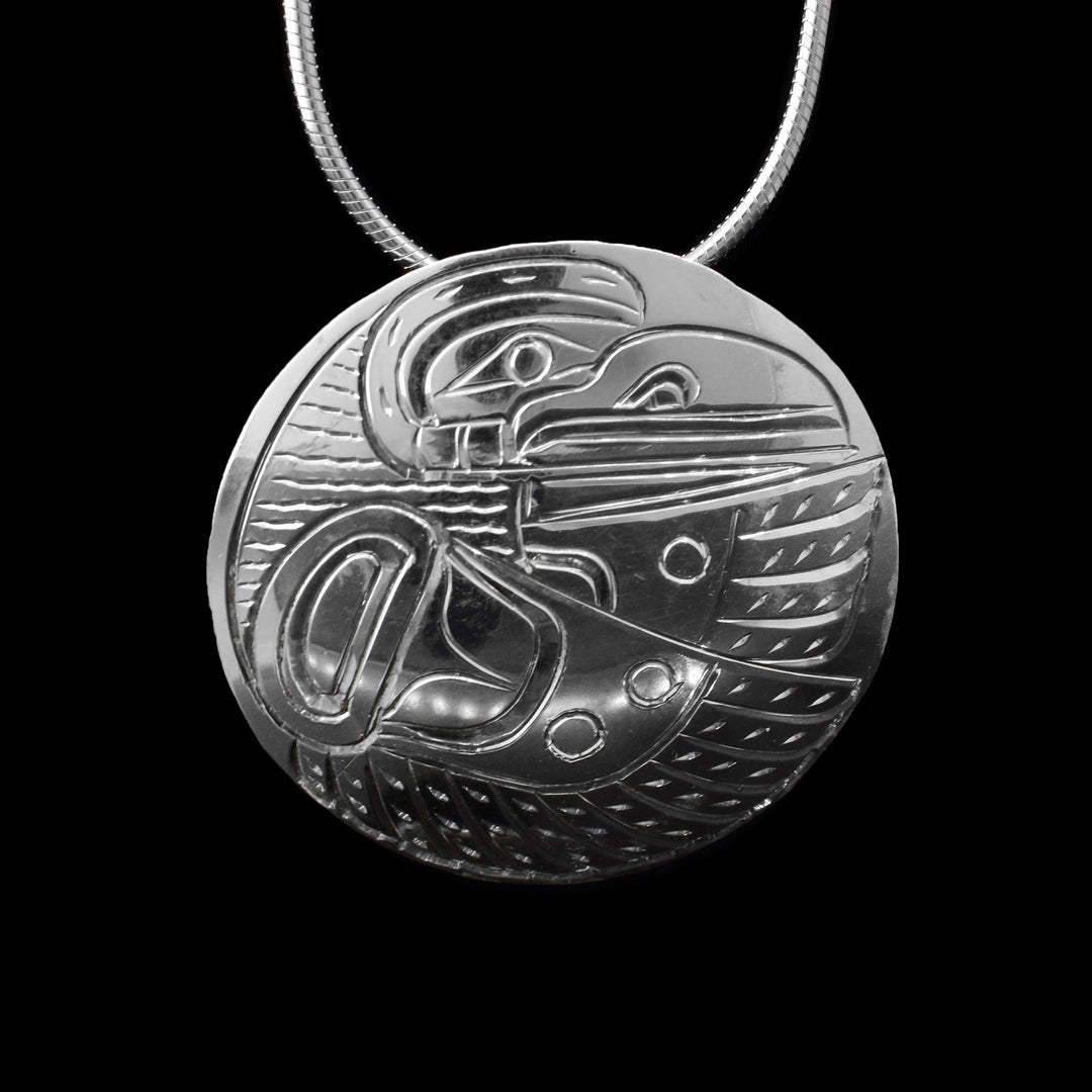 This sterling silver Raven pendant is circular in shape and has engravings that depict the left profile side of a raven. Two wings reach out to the left side.