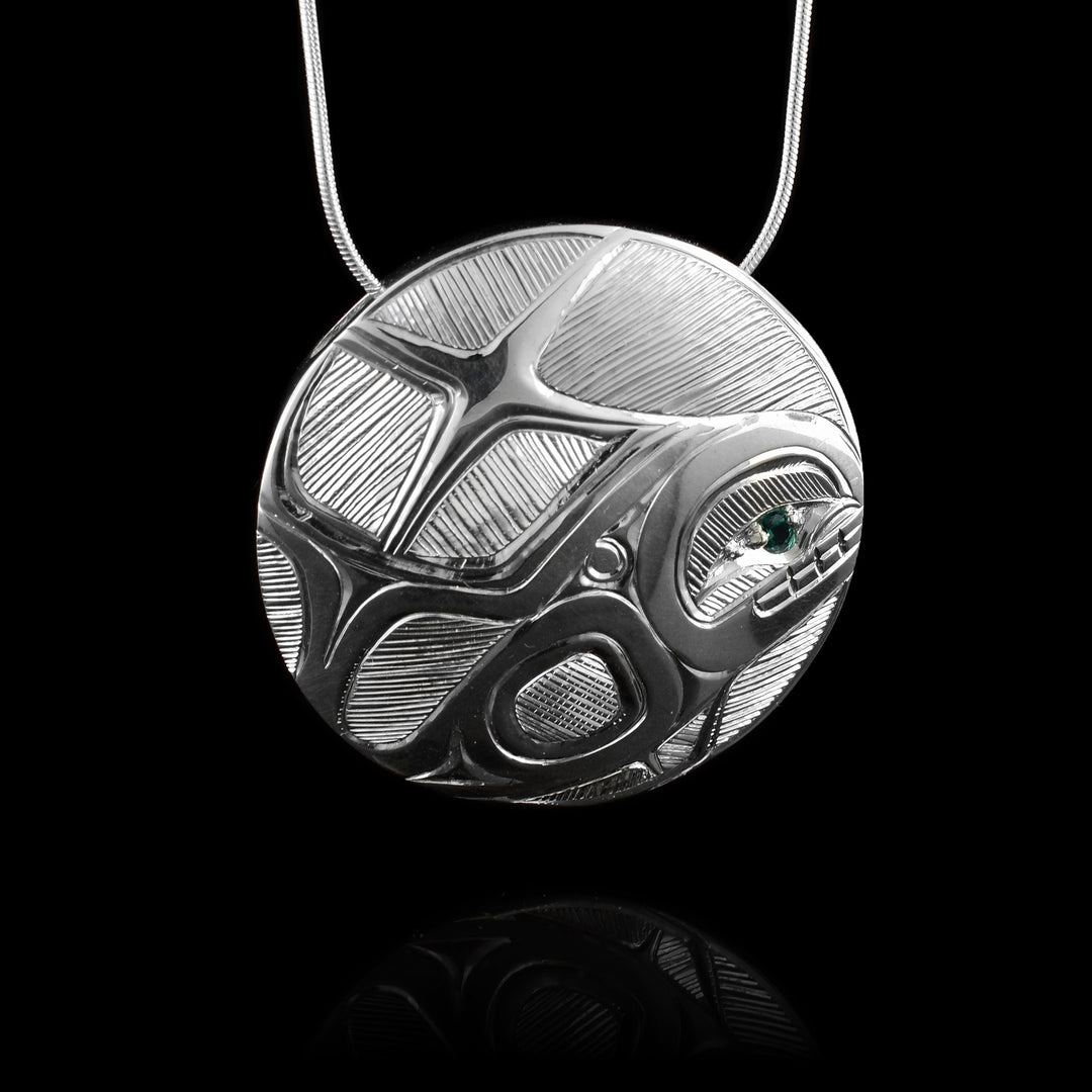 This circular whale pendant is made with sterling silver with a hand-carved legend of the whale with an emerald in the whales eye. 