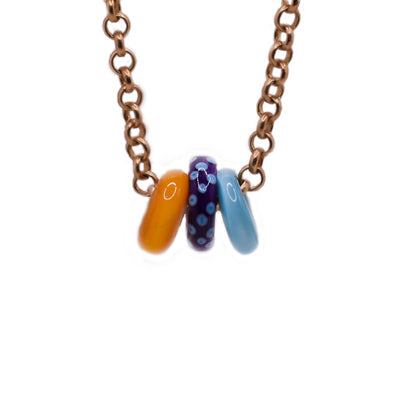 Gold-plated chain with three handmade lampworked glass rings, in orange, purple with blue dots and blue. By Wendy Pierson.