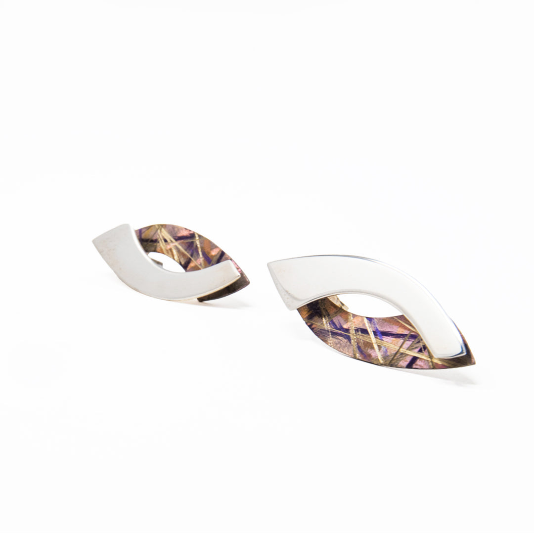 These unique titanium stud earrings are made form sterling silver and anodized titanium. The pieces have a vertical, oval shape and combines a silver and a titanium band with a gap in the middle between them. There are brilliant colors and designs on the surface on the titanium sections achieved by anodizing the metal.