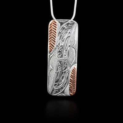 Sterling silver bear pendant featuring a bear facing downwards from top and another facing upwards from bottom. Two copper feathers. Hand-carved by Kwakwaka’wakw artist Cristiano Bruno.