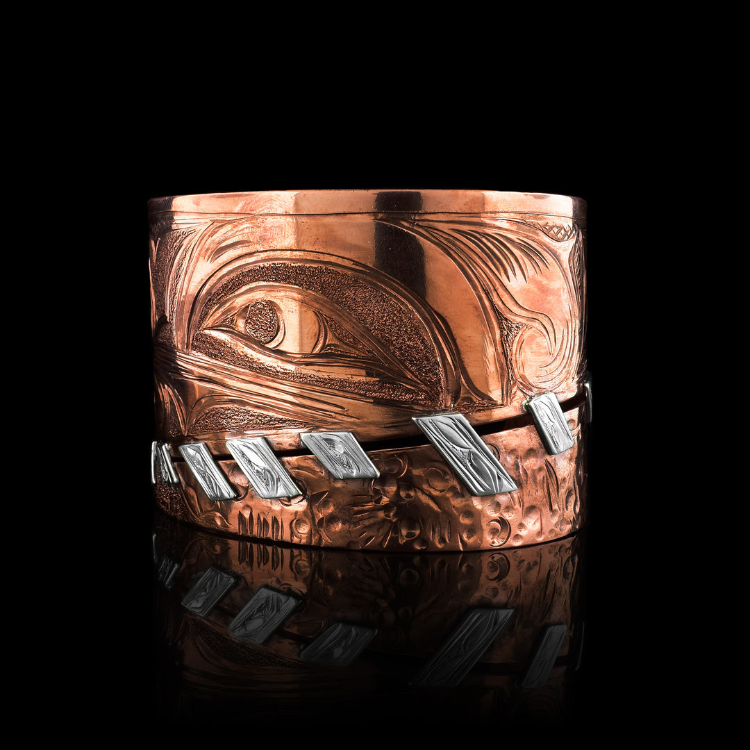 Artisan Hummingbird Wrap Bracelet by Cristiano Bruno. Expertly hand-carved in copper with sterling silver accents stiches diagonally along the bottom, this Kwakwaka'wakw statement piece showcases traditional Indigenous design in a unique.