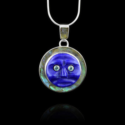 This lapis lazuli pendant is made from a sterling silver circle and has abalone mounted on it. There is a circle shaped, lapis lazuli gem that is carved to depict the moon and is has blue topaz gems as its eyes.