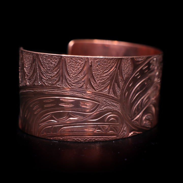 This stunning Bear bracelet is made using copper and has a single, wide band with a gap in the back. There are intricate carvings on the surface of the piece that depicts the Baby Bear in the womb and being watched over by its mother who is depicted in silver and carved on the side of the piece. On the other side of the band, there are depictions of trees.