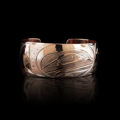 This copper cuff bracelet has a single, side band with a gap in the back. There is a baby Orca depicted in the womb with its mother watching over is on one side of the piece and a two dorsal fins in the ocean depicted on the other side. This piece represents family and community.