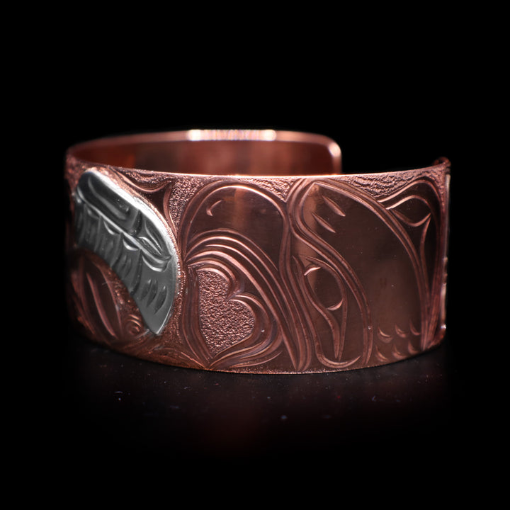 This Eagle bracelet has a wide band made from copper and with a gap in the back. There is a depiction of a baby eagle with its wing made from sterling silver being watched over by its mother carved into the band.