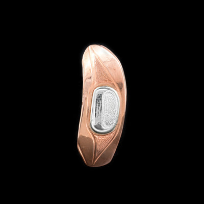 This sterling silver and copper brooch pin has a round, vertical shape. The piece depicts an egg of the Salmon and has carvings on the surface on it depicting the egg.