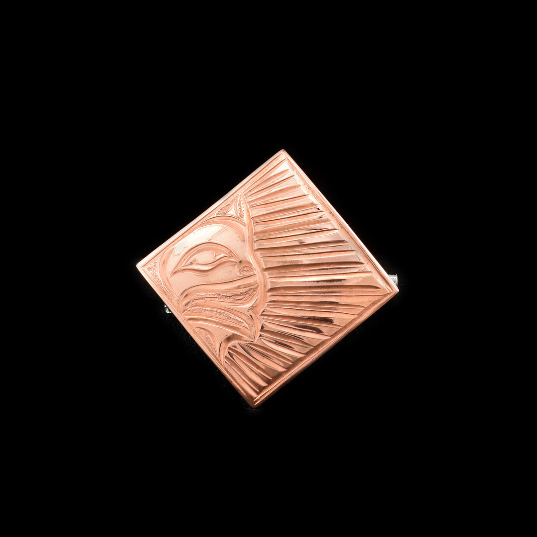 This Sun brooch is made from copper and is diamond shaped. There are carvings on the surface of the pin that depict the Sun in the corner with rays shining from it.