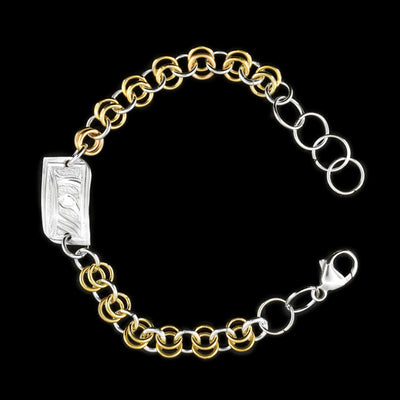 This silver and gold link bracelet is made from sterling silver and 14K gold fill. This piece has a silver and gold fill chain with a rectangle charm at the top. There is a depiction of the Moon carved into the surface of the silver charm.