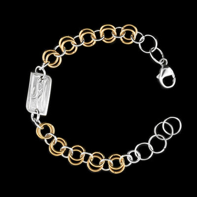 this silver and gold link bracelet is made from sterling silver and 14K gold fill. This piece has a silver and gold fill chain with a rectangle charm at the top. There is a depiction of the Raven carved into the surface of the silver charm.
