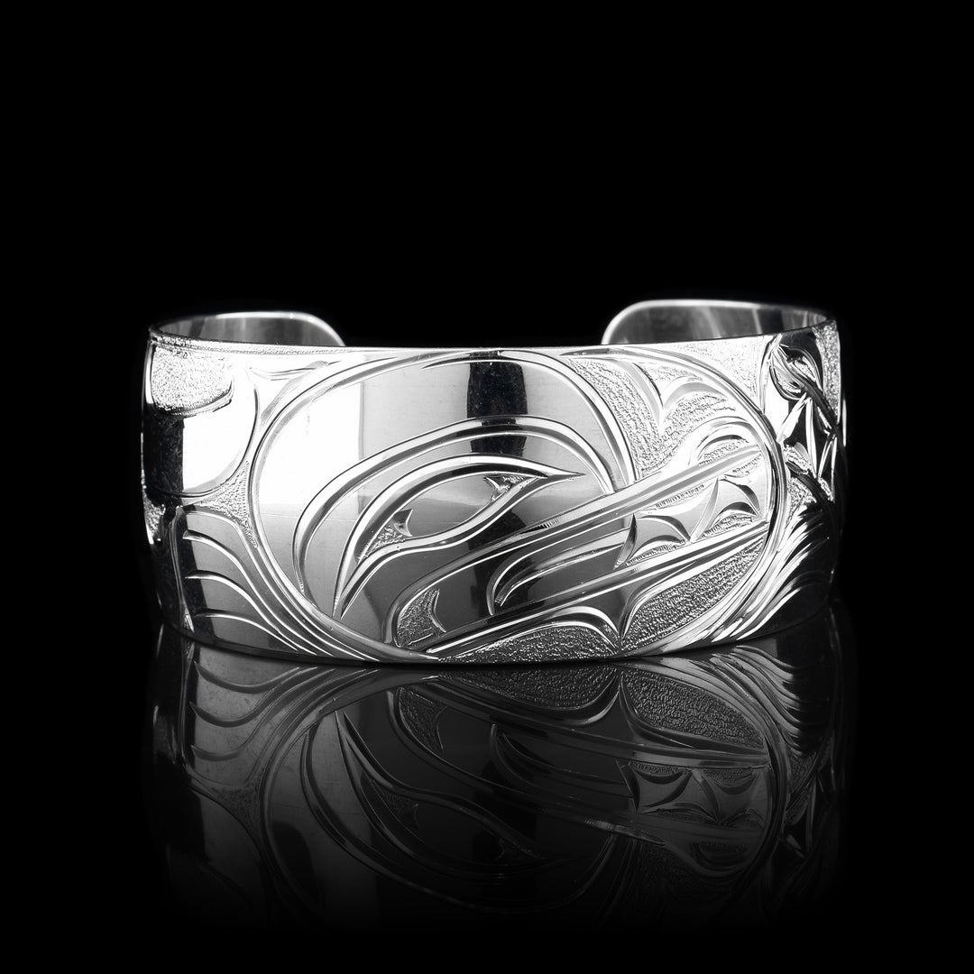 This stunning Wolf bracelet is made using sterling silver and has a single, wide band with a gap in the back. There are intricate carvings on the surface of the piece that depicts the Baby Wolf in the womb and being watched over by its mother who is depicted in silver and carved on the side of the piece. On the other side of the band, the tail of the mother Wolf is depicted..