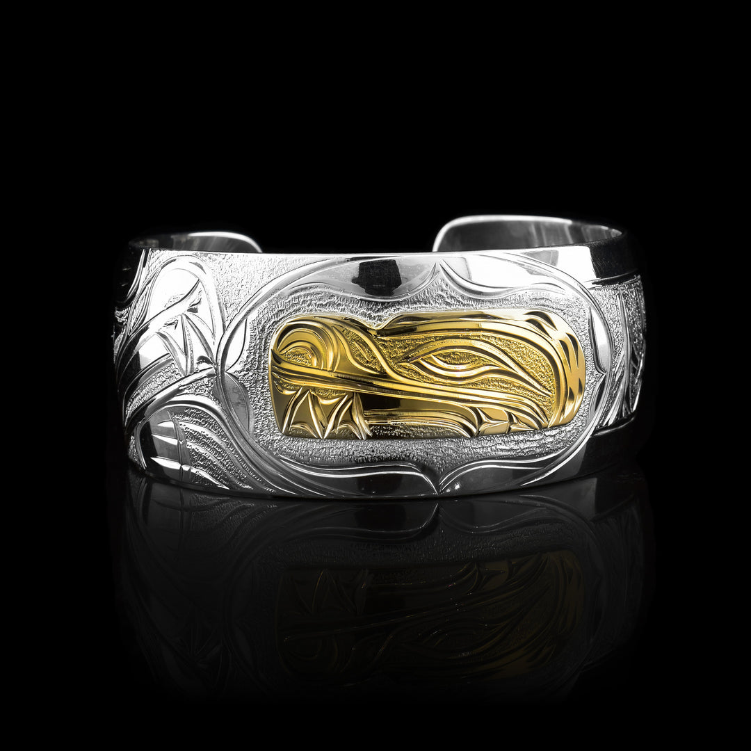 This stunning Bear bracelet is made using sterling silver, 14K gold and has a single, wide band with a gap in the back. There are intricate carvings on the surface of the piece that depicts the Baby Bear, done in gold, in the womb and being watched over by its mother who is depicted in silver and carved on the side of the piece. On the other side of the band, there are depictions of forest trees.