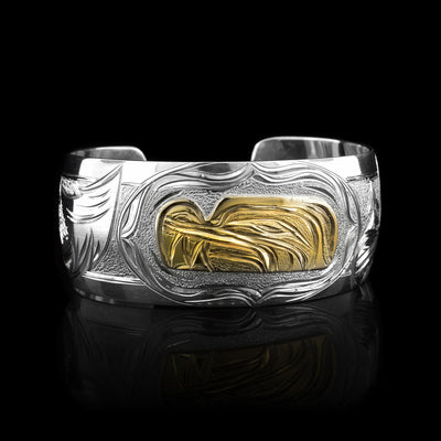 This stunning Wolf bracelet is made using sterling silver, 14K gold and has a single, wide band with a gap in the back. There are intricate carvings on the surface of the piece that depicts the Baby Wolf, done in gold, in the womb and being watched over by its mother who is depicted in silver and carved on the side of the piece. On the other side of the band, the tail of the Mother Wolf is depicted.