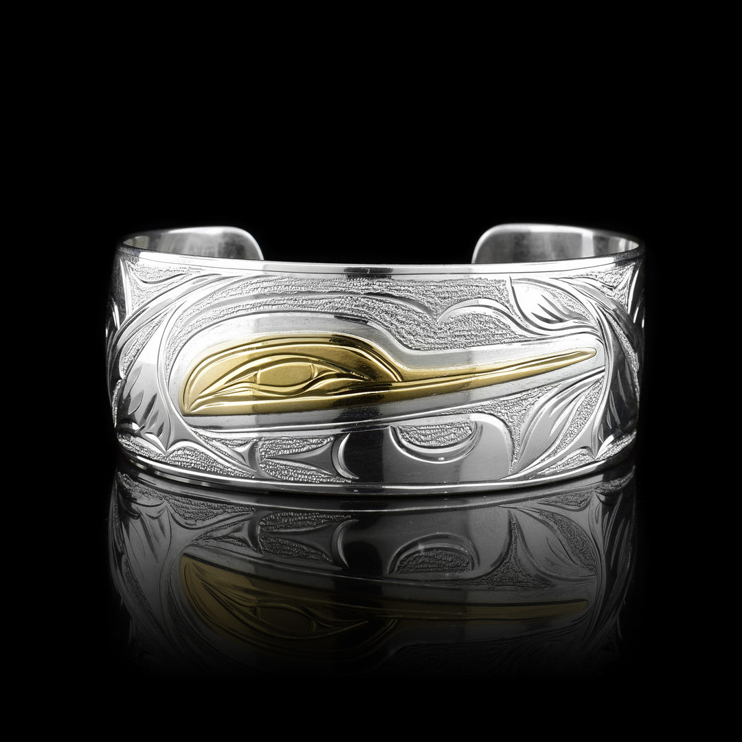 This Hummingbird bracelet has been made with sterling silver and 14K gold with a single wide band and a gap in the back. There are carvings on the surface of the band depicting the Hummingbird. The head of the legend is made form gold.