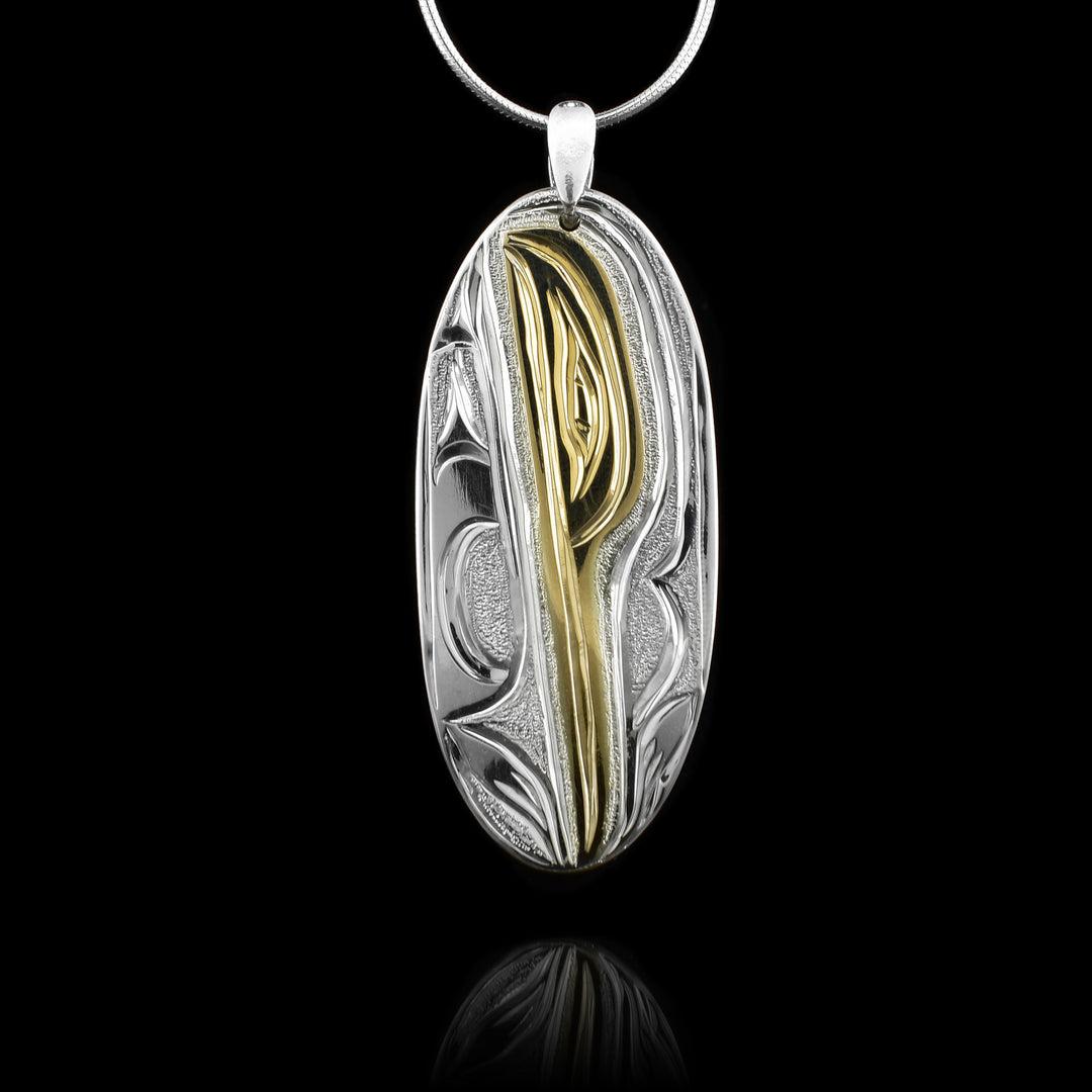 This Hummingbird pendant is made from sterling silver and 14K gold with a long, oval shape. There is a depiction of the Hummingbird carved into the surface of the pendant and the head of the legend is done in gold.