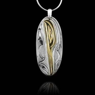 This Hummingbird pendant is made from sterling silver and 14K gold with a long, oval shape. There is a depiction of the Hummingbird carved into the surface of the pendant and the head of the legend is done in gold.