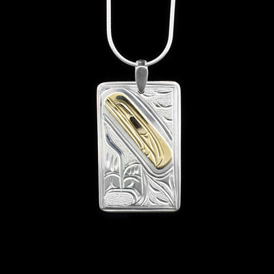 This Orca pendant is made from sterling silver, 14K gold and has a large, rectangular shape. There is a depiction of the Orca and designs carved into the surface of the piece and they head of the Orca is made from 14K gold.