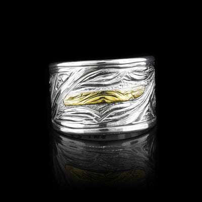 This Orca ring has a wide sterling silver band that has wavy designs and carvings made across the surface of the band. There is a depiction of the Orca made from 14K gold that is carved into the band. The Orca is a small rectangle with details made in it. 