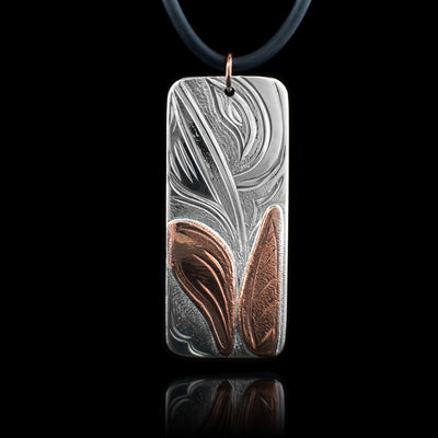 This Hummingbird pendant is made from sterling silver and is large and rectangle shaped. There are carvings across the surface of it depicting the Hummingbird dipping into a flower that is made from copper.