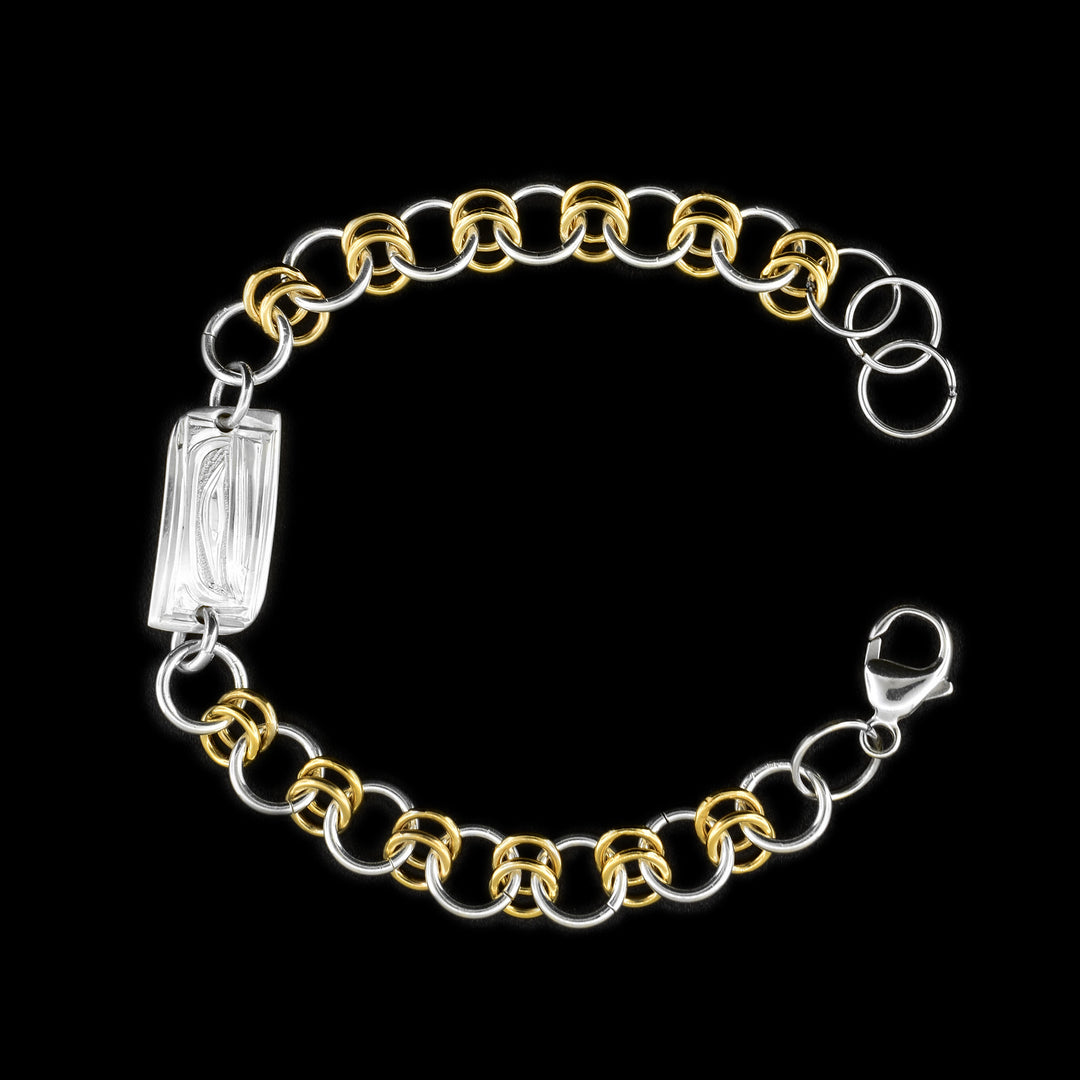 this silver and gold link bracelet is made from sterling silver and 14K gold fill. This piece has a silver and gold fill chain with a rectangle charm at the top. There is a depiction of the Orca carved into the surface of the silver charm.