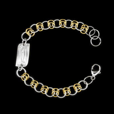 this silver and gold link bracelet is made from sterling silver and 14K gold fill. This piece has a silver and gold fill chain with a rectangle charm at the top. There is a depiction of the Orca carved into the surface of the silver charm.