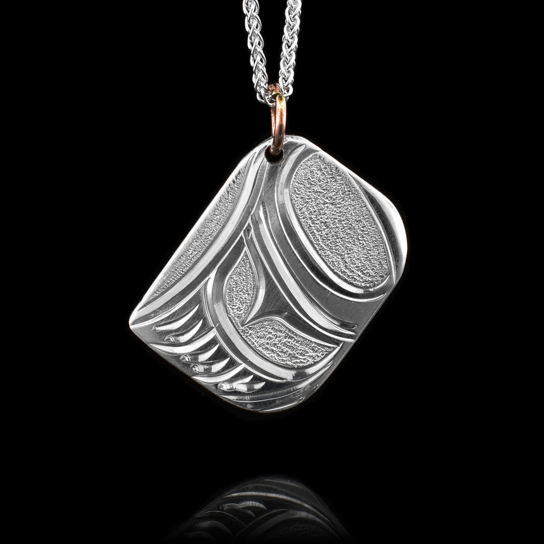 This feather pendant is square shaped and made from sterling silver. The pendant dangles from a copper jump ring. The designs resemble that of a feather that is done in an indigenous art style and there are textured dimples in the blank spaces of the piece.