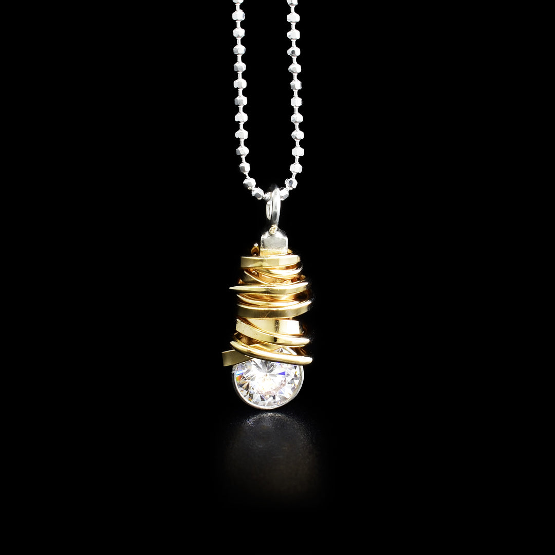 Pendant hangs from sterling silver ball chain. Sterling silver pendant has gold-fill coil wrapped around, ending at cubic zirconia on bottom.