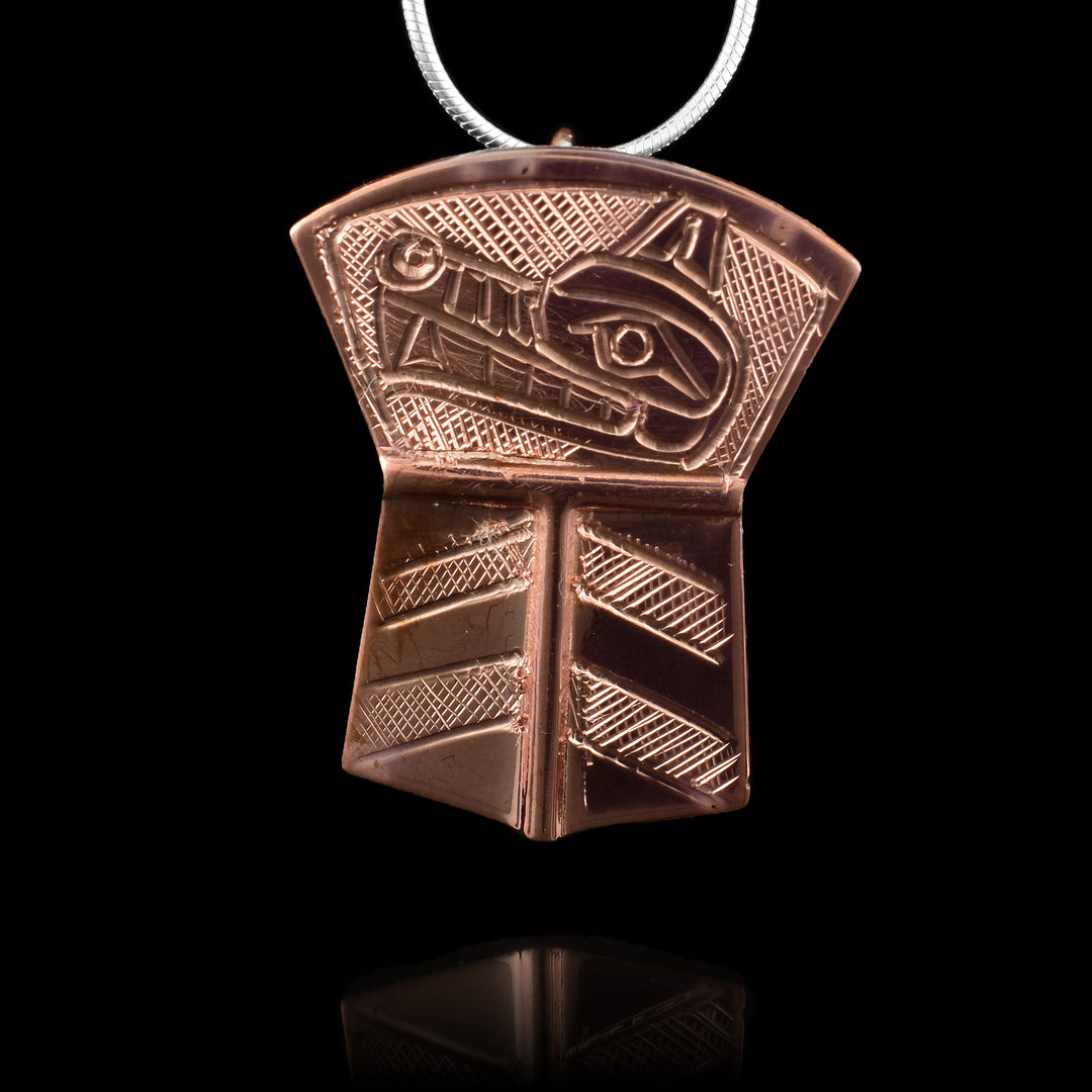 This copper Wolf pendant is shaped like a shield with the top flaring out and the bottom dropping down in a rectangular shape. At the top portion, there is a side profile depiction of the head of the Wolf with its eye, mouth, nose and teeth detailed. There are cross hatching bands on the bottom portion and in the background of the top of the piece.